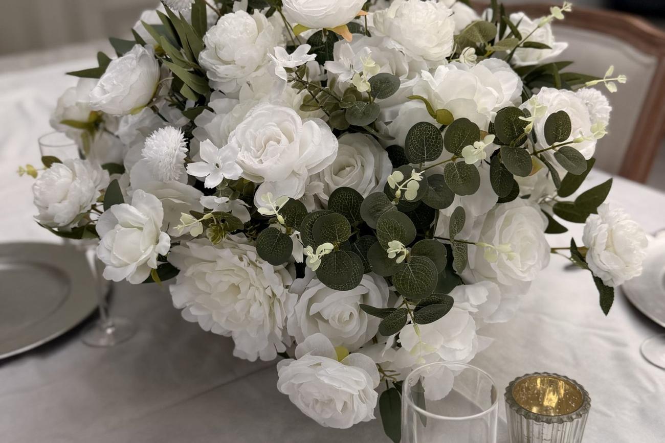 An ivory and eucalyptus centrepiece on a dressed table, with a silver charger and a gold tealight